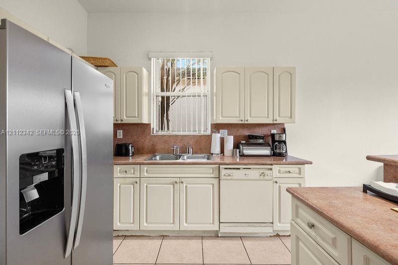 Kitchen featuring off-white cabinetry, stainless steel side-by-side refrigerator, tile backsplash, solid-surface countertops, and ceramic tile flooring