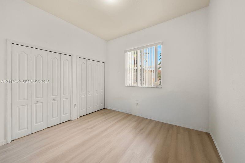 Interior space featuring light-toned wood-finish flooring, dual sets of white paneled bifold closet doors, and a window with vertical blinds