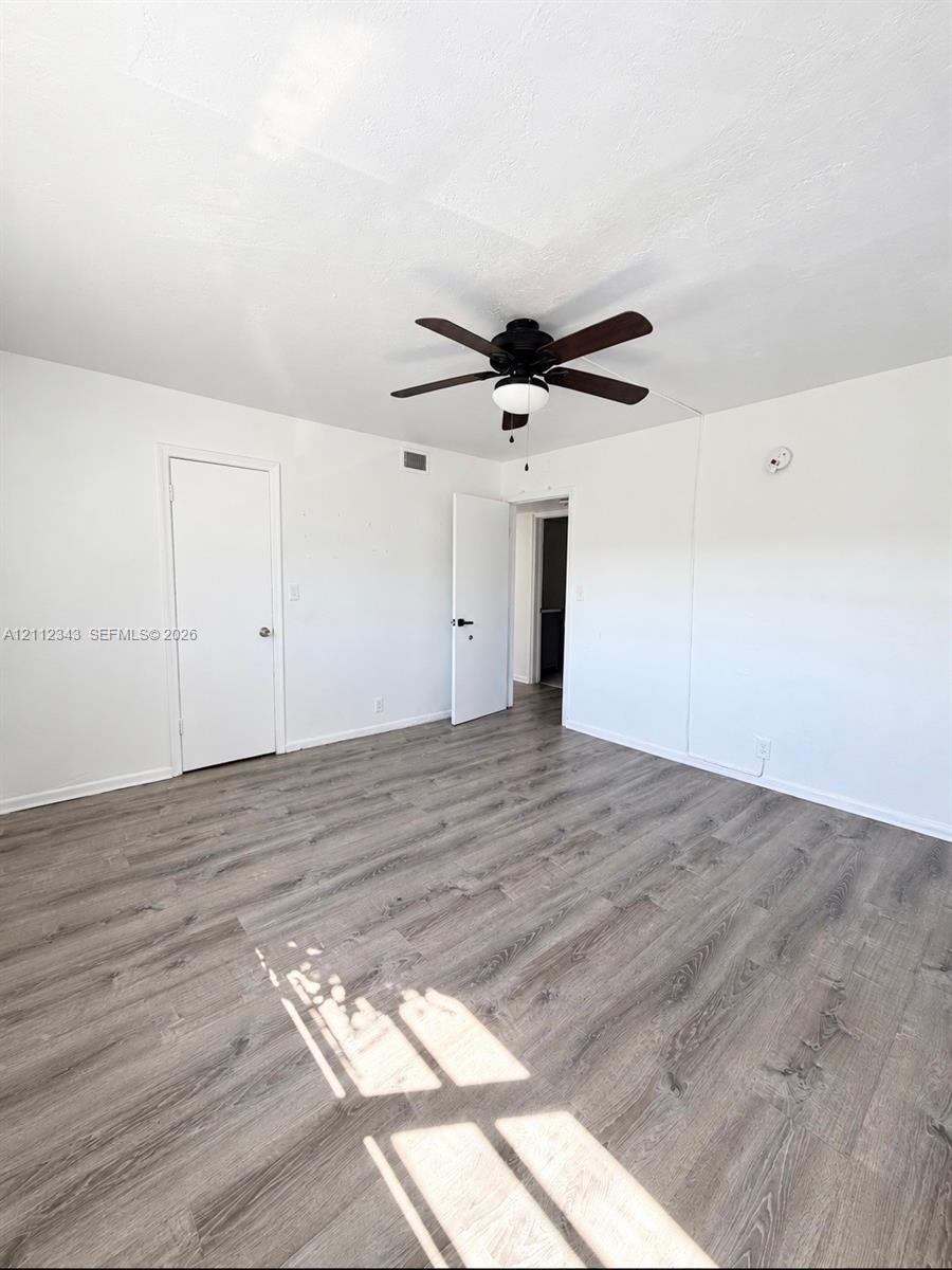 Interior room featuring wood-finish flooring, a multi-blade ceiling fan with integrated lighting, and two doors