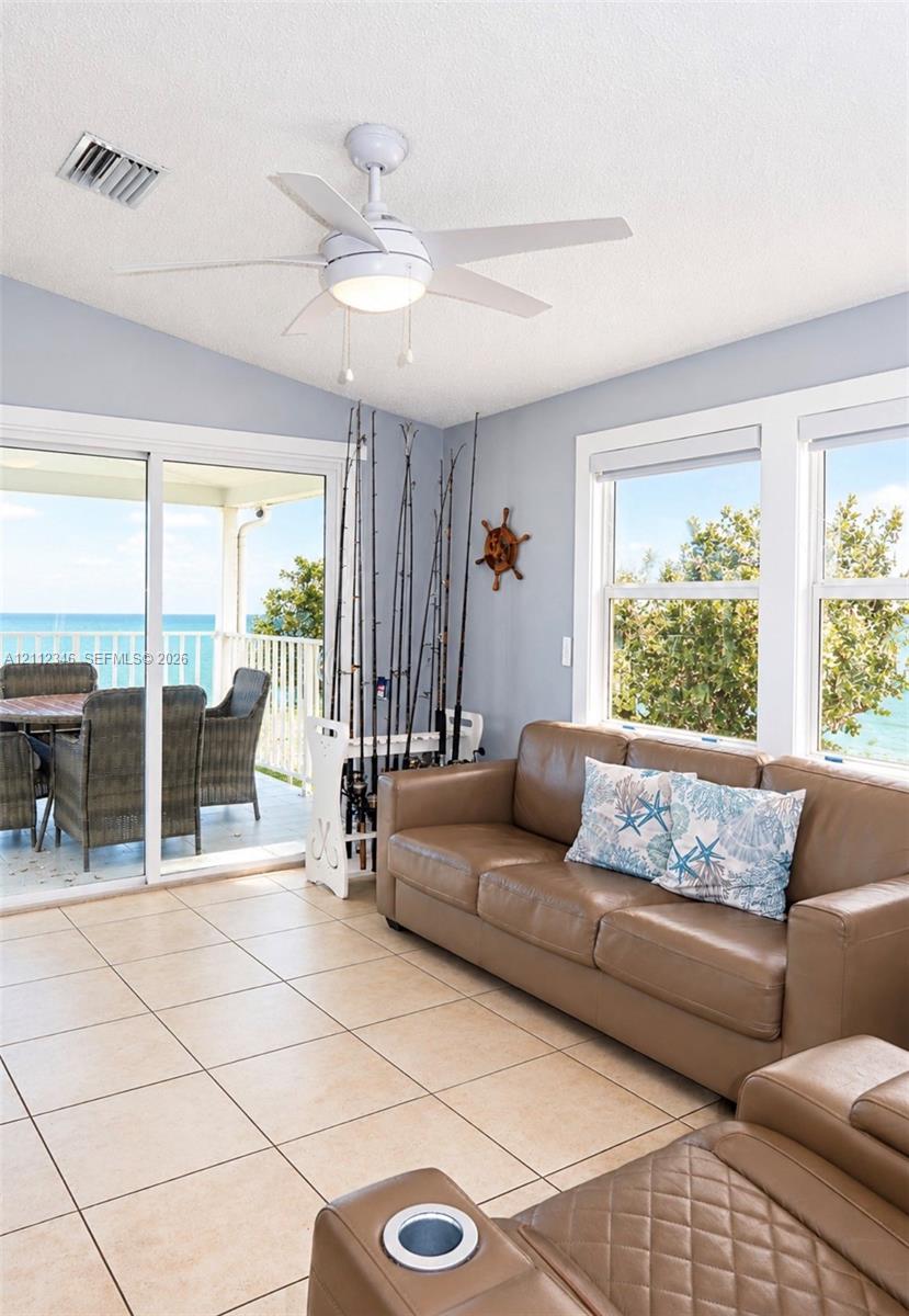 Sunroom featuring vaulted ceilings, ceramic tile flooring, a white ceiling fan with integrated lighting, and sliding glass doors with exterior water scenery Sunroom featuring vaulted ceilings, ceramic tile flooring, a white ceiling fan with integrated lighting, and sliding glass doors with exterior water scenery