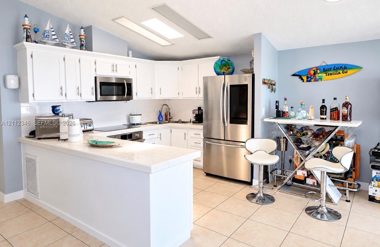 Kitchen featuring white cabinetry, tile countertops, stainless steel appliances, and tile flooring Kitchen featuring white cabinetry, tile countertops, stainless steel appliances, and tile flooring