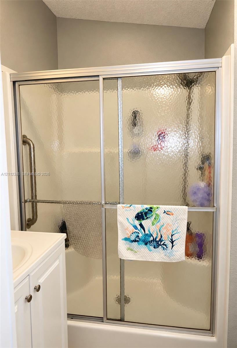 Tub-shower combination featuring a white surround, sliding textured glass doors, and a chrome grab bar