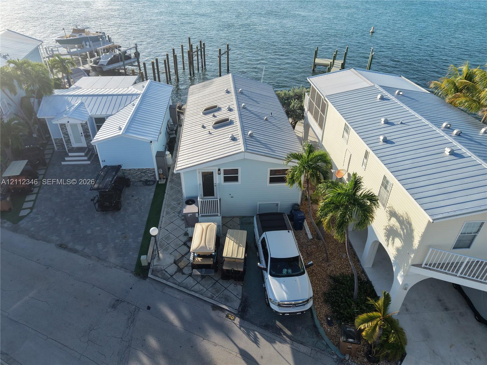 Waterfront property featuring a private boat dock, metal roofing, paved driveway, and palm-lined exterior landscaping