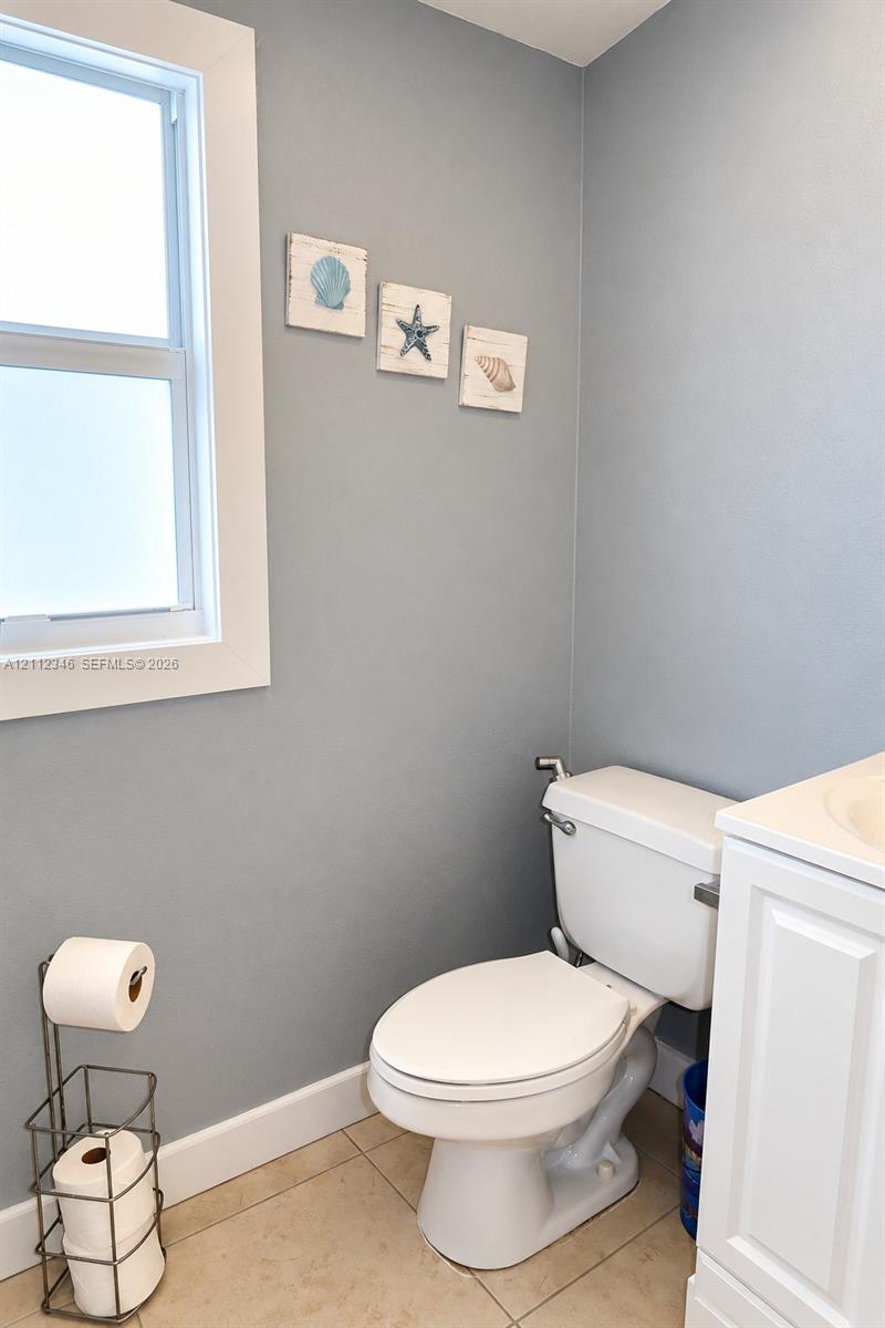 Single-hung window with white casing, neutral grey walls, ceramic tile flooring, and white vanity cabinetry
