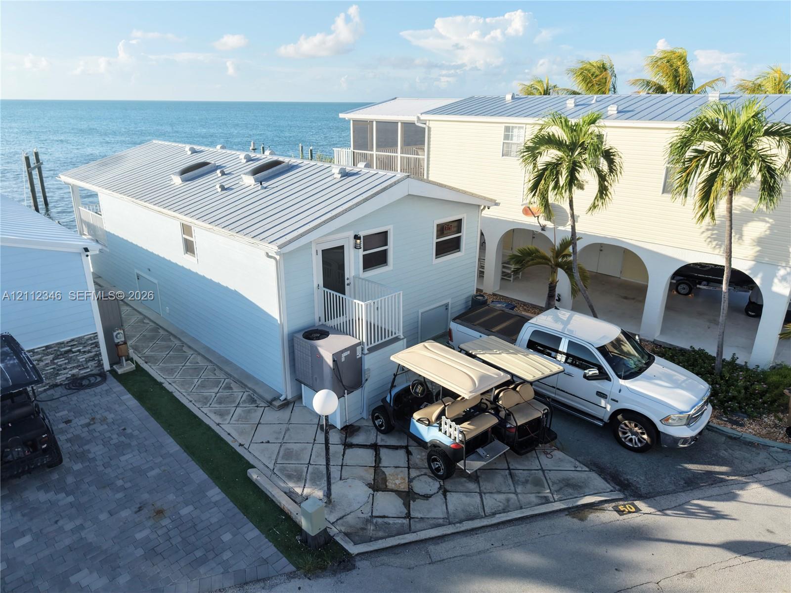 Waterfront property exterior featuring metal roofing, skylights, horizontal siding, and a paved parking area Waterfront property exterior featuring metal roofing, skylights, horizontal siding, and a paved parking area