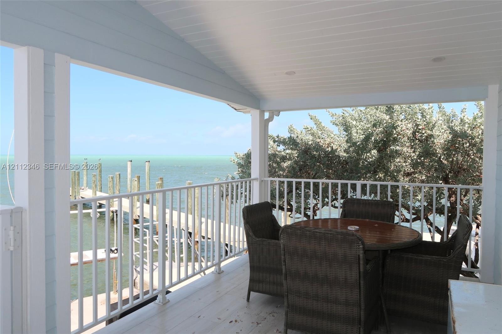 Sliding glass door opening to a covered balcony with a white metal railing, tile flooring, and coastal water backdrop