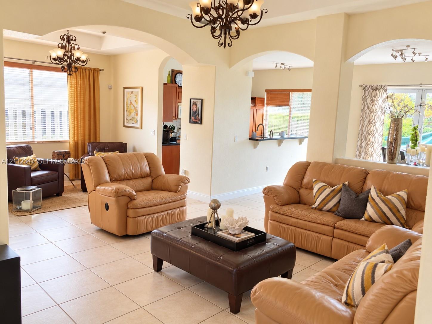 Open-concept interior featuring arched wall openings, large-format tile flooring, tiered ceiling detail, and wrought-iron style chandelier fixtures