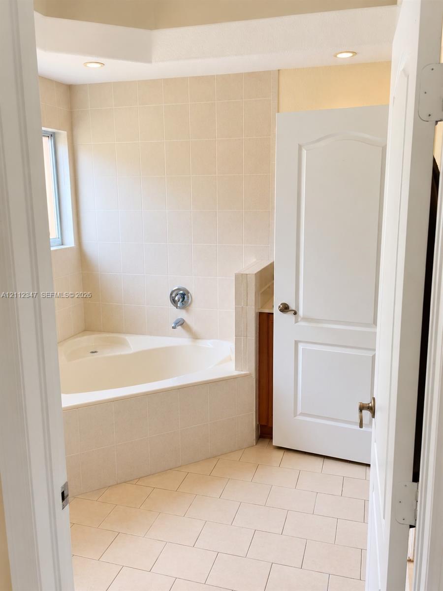 Corner soaking tub featuring ceramic tile surround, recessed lighting, and tile flooring
