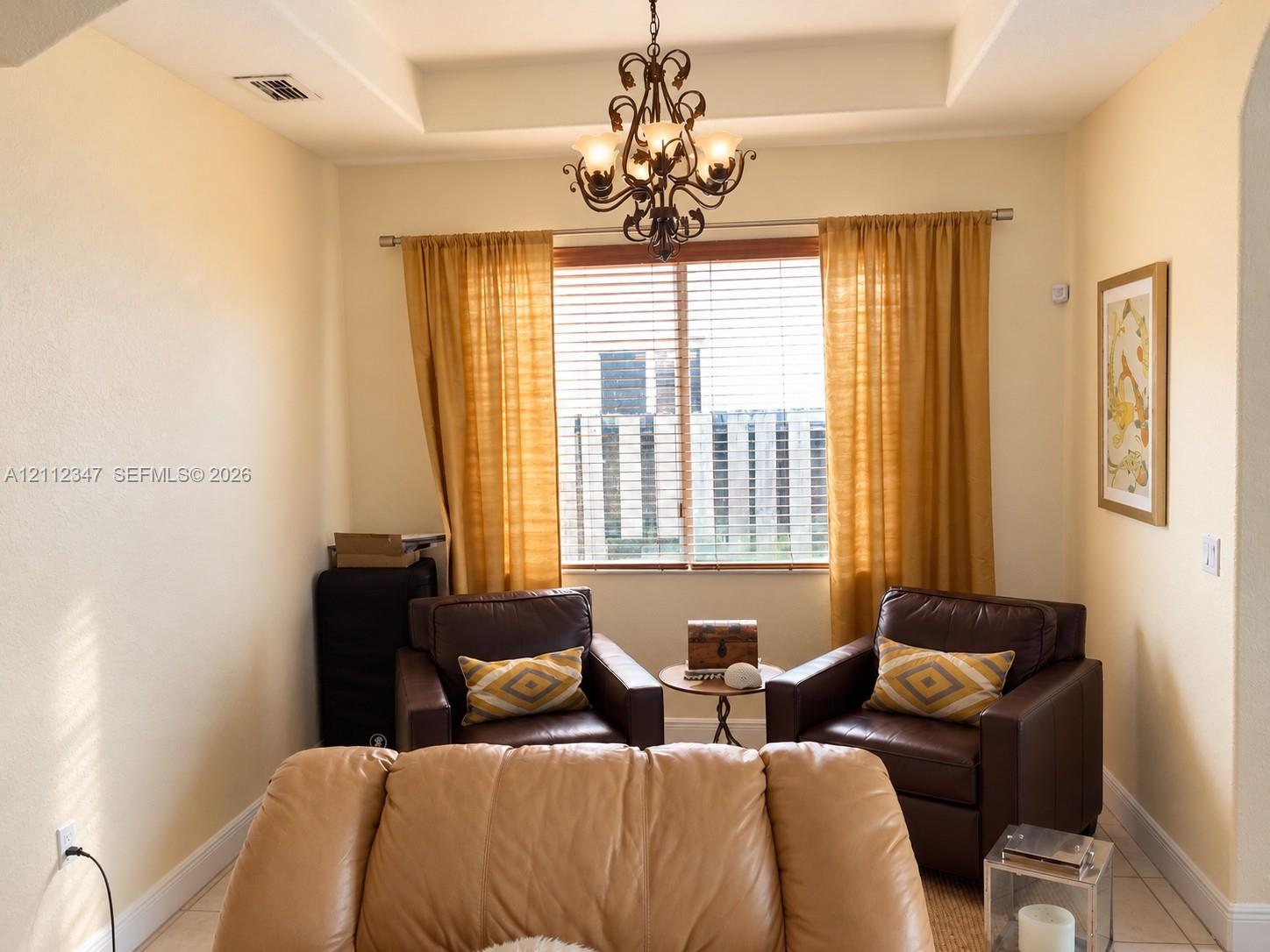 Interior space featuring a recessed tray ceiling, wrought-iron chandelier, and horizontal window blinds