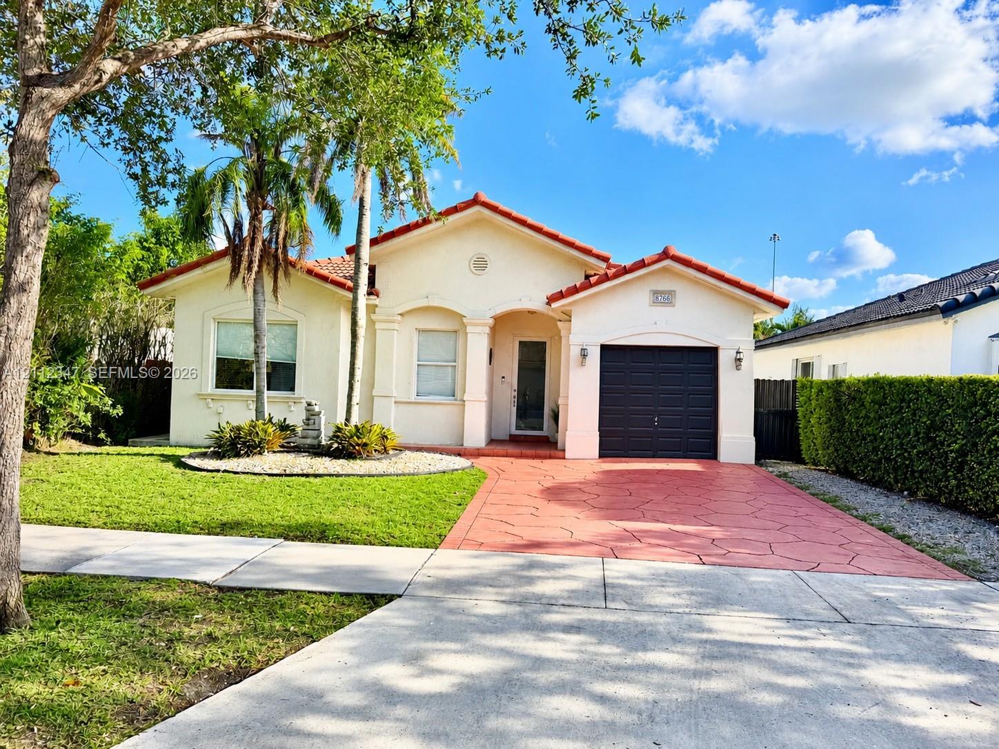 Stucco exterior with a tiled roof, arched entryway, stamped concrete driveway, and attached single-car garage
