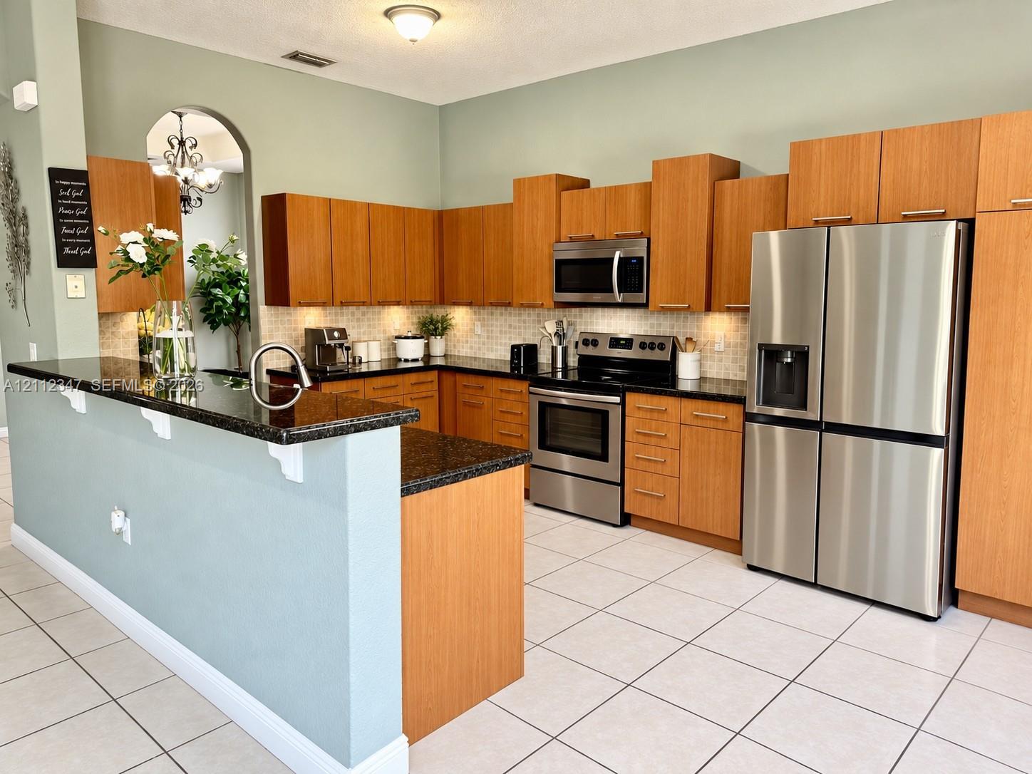 Kitchen featuring wood cabinetry, stone countertops, stainless steel appliances, tiled backsplash, and a breakfast bar
