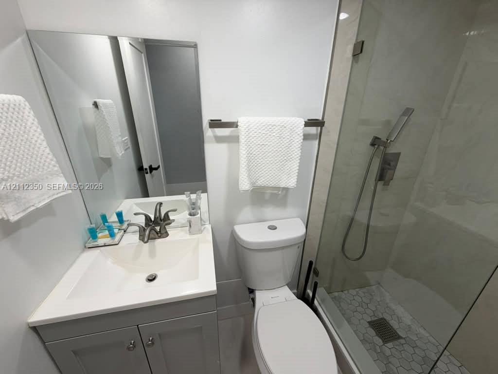 Bathroom featuring a gray shaker-style vanity with a solid-surface integrated sink, frameless glass shower enclosure, handheld shower fixture, and hexagonal floor tile