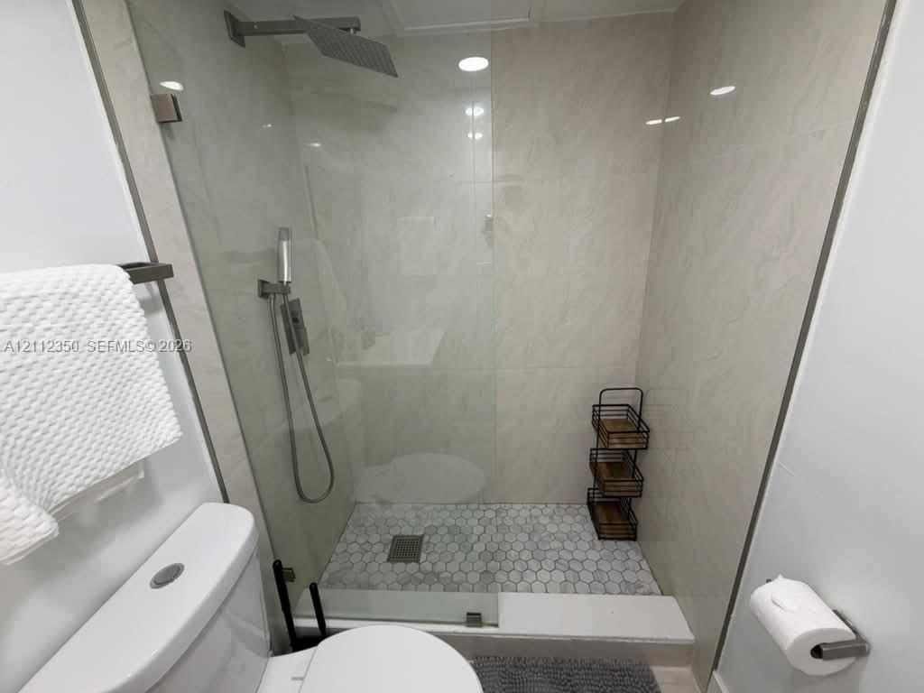 Walk-in shower featuring large-format wall tile, hexagonal floor tile, glass enclosure, and ceiling-mounted rain showerhead with a secondary handheld sprayer