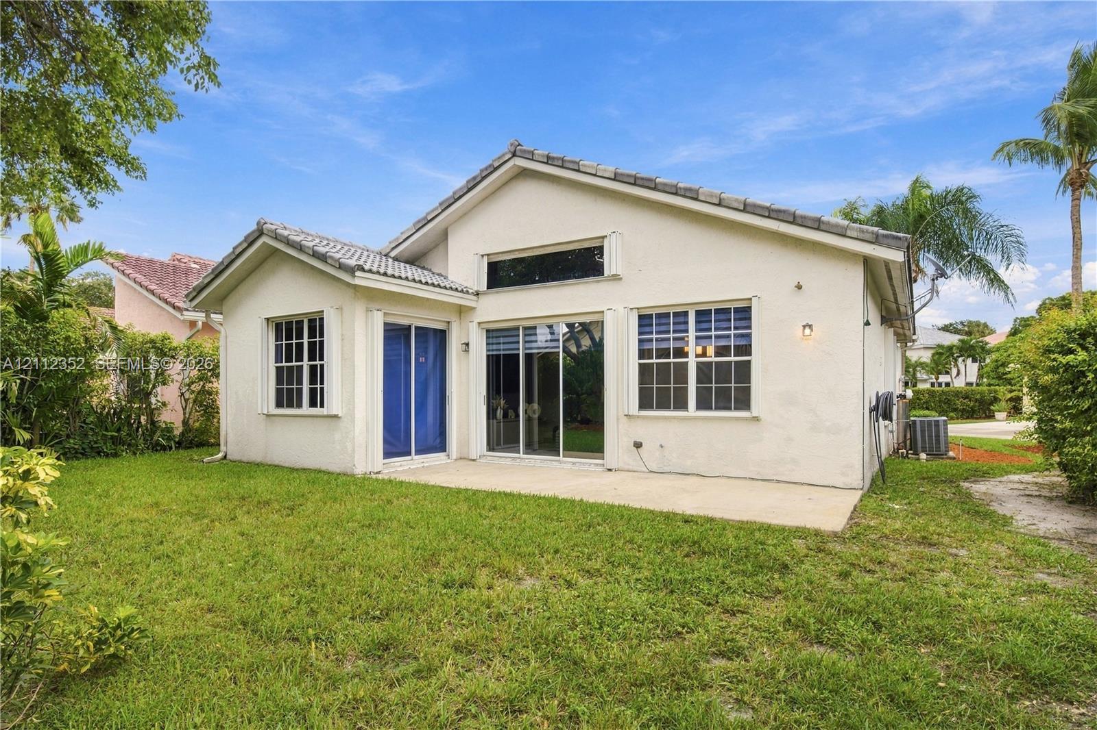 Stucco exterior featuring a concrete tile roof, rear concrete patio, sliding glass doors, and a multi-paned transom window