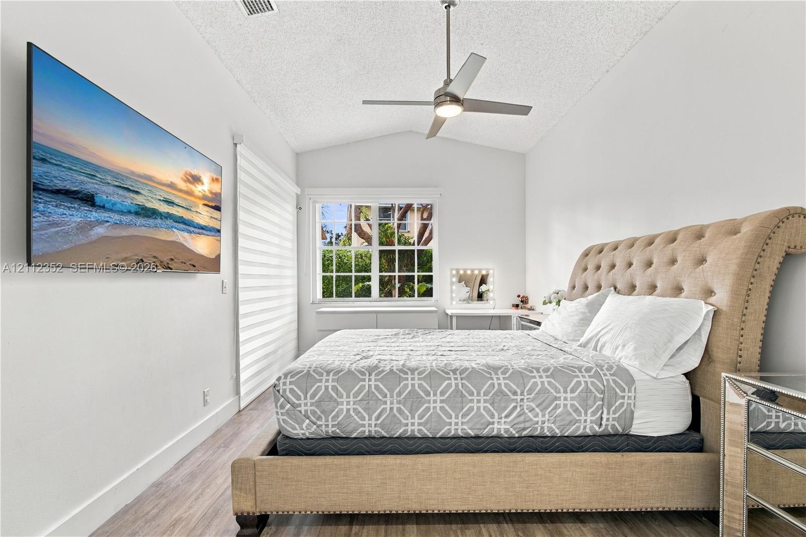 Vaulted ceiling featuring a central brushed-metal ceiling fan, wood-finish flooring, and a multi-pane window