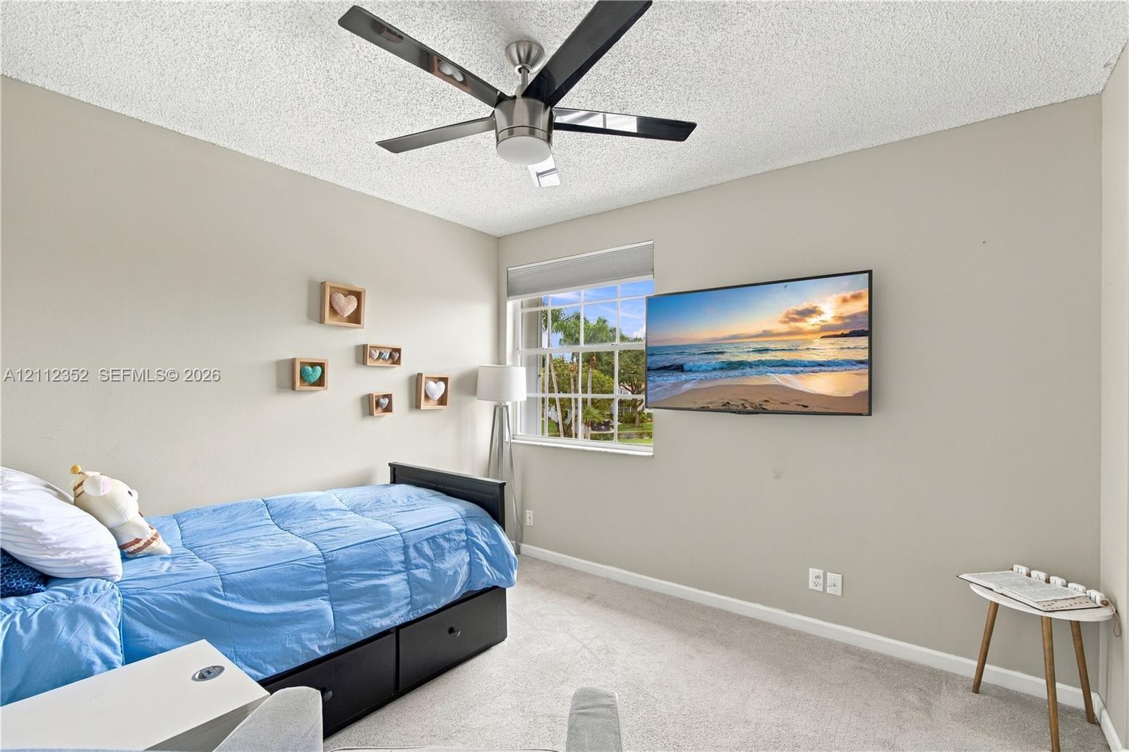 Room featuring a brushed-nickel ceiling fan with dark-toned blades, neutral wall paint, carpeting, and a grid-pattern window