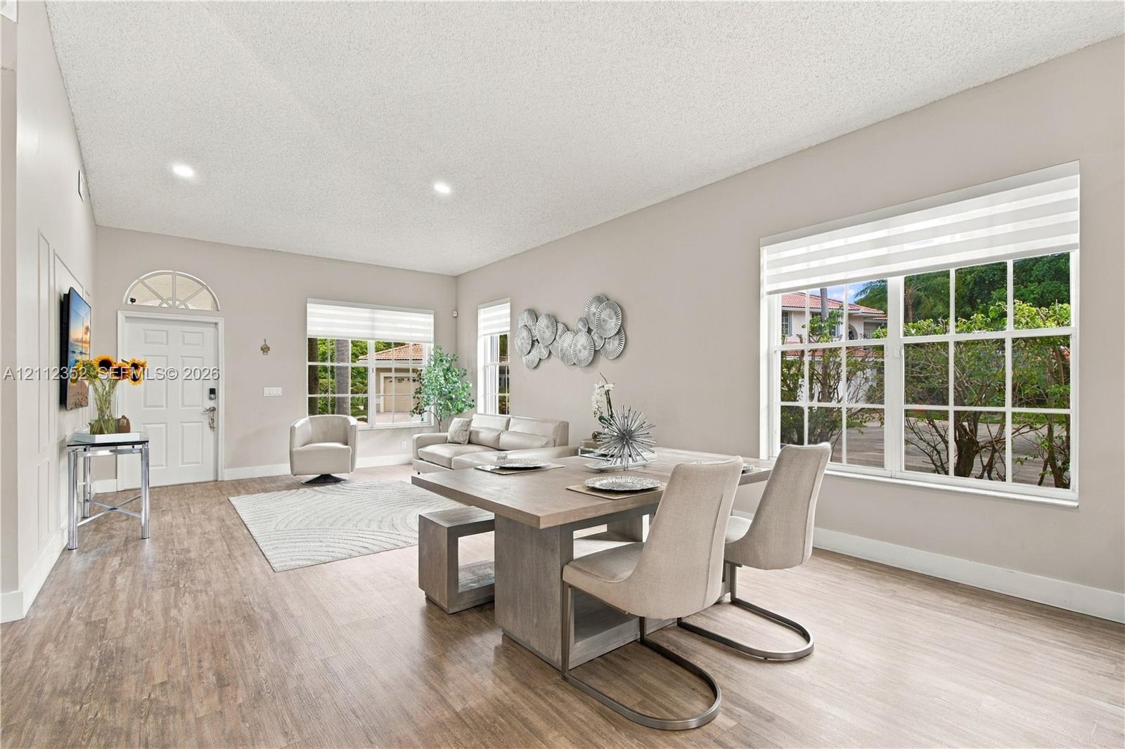 Open-concept living space featuring wood-finish flooring, recessed lighting, multiple oversized windows, and a front entry door with a transom window Open-concept living space featuring wood-finish flooring, recessed lighting, multiple oversized windows, and a front entry door with a transom window