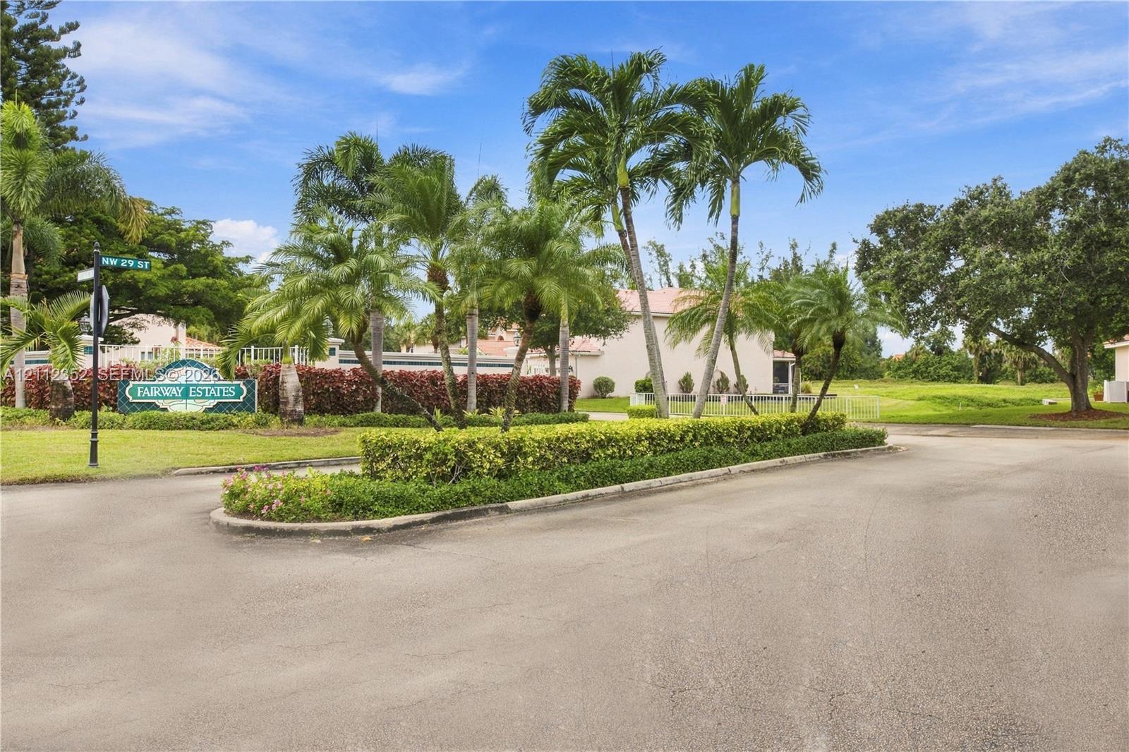 Entryway featuring mature palm trees, manicured hedges, paved roadways, and ornamental shrubbery Entryway featuring mature palm trees, manicured hedges, paved roadways, and ornamental shrubbery