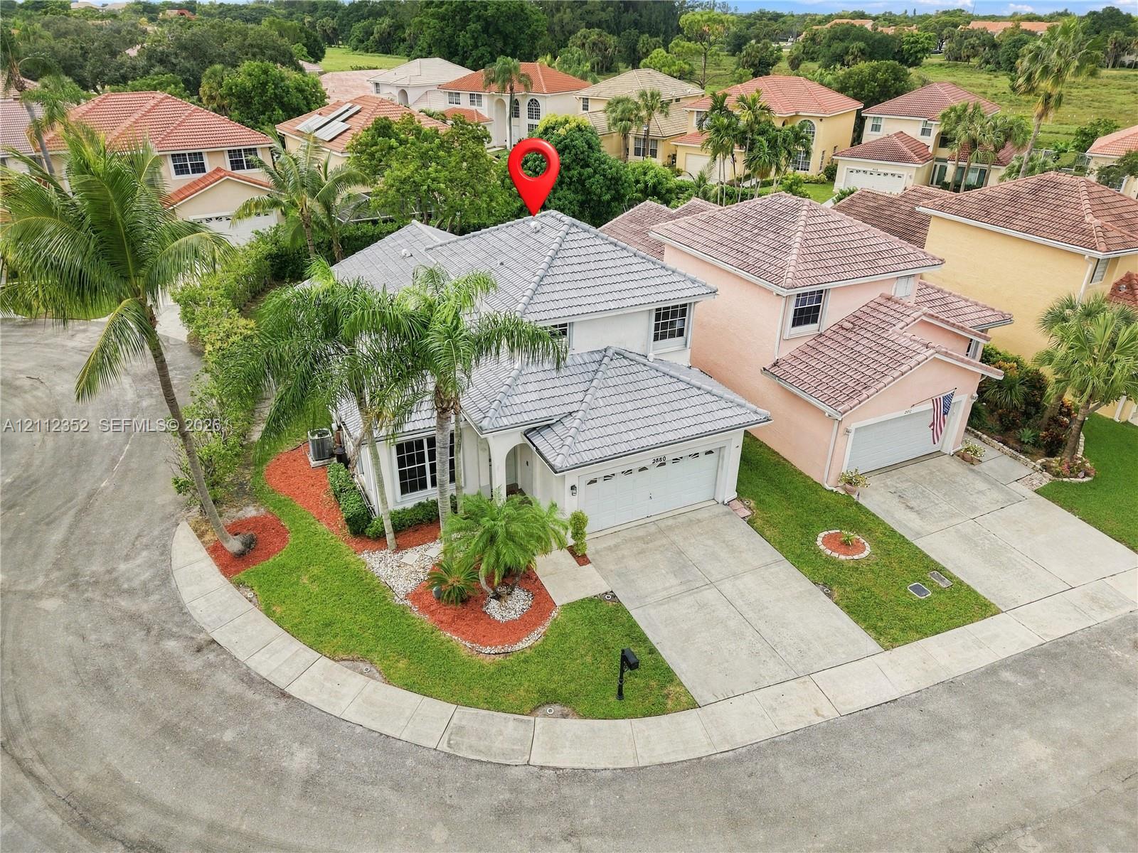 Two-story residence featuring a concrete tile roof, attached two-car garage, concrete driveway, and established palm tree landscaping