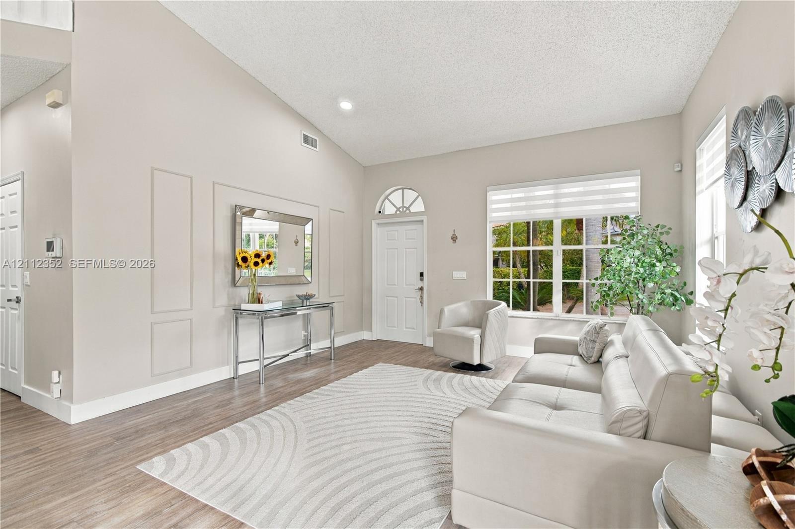 Living room featuring vaulted ceilings, wood-finish flooring, wall molding detail, and a front entry door with a transom window Living room featuring vaulted ceilings, wood-finish flooring, wall molding detail, and a front entry door with a transom window
