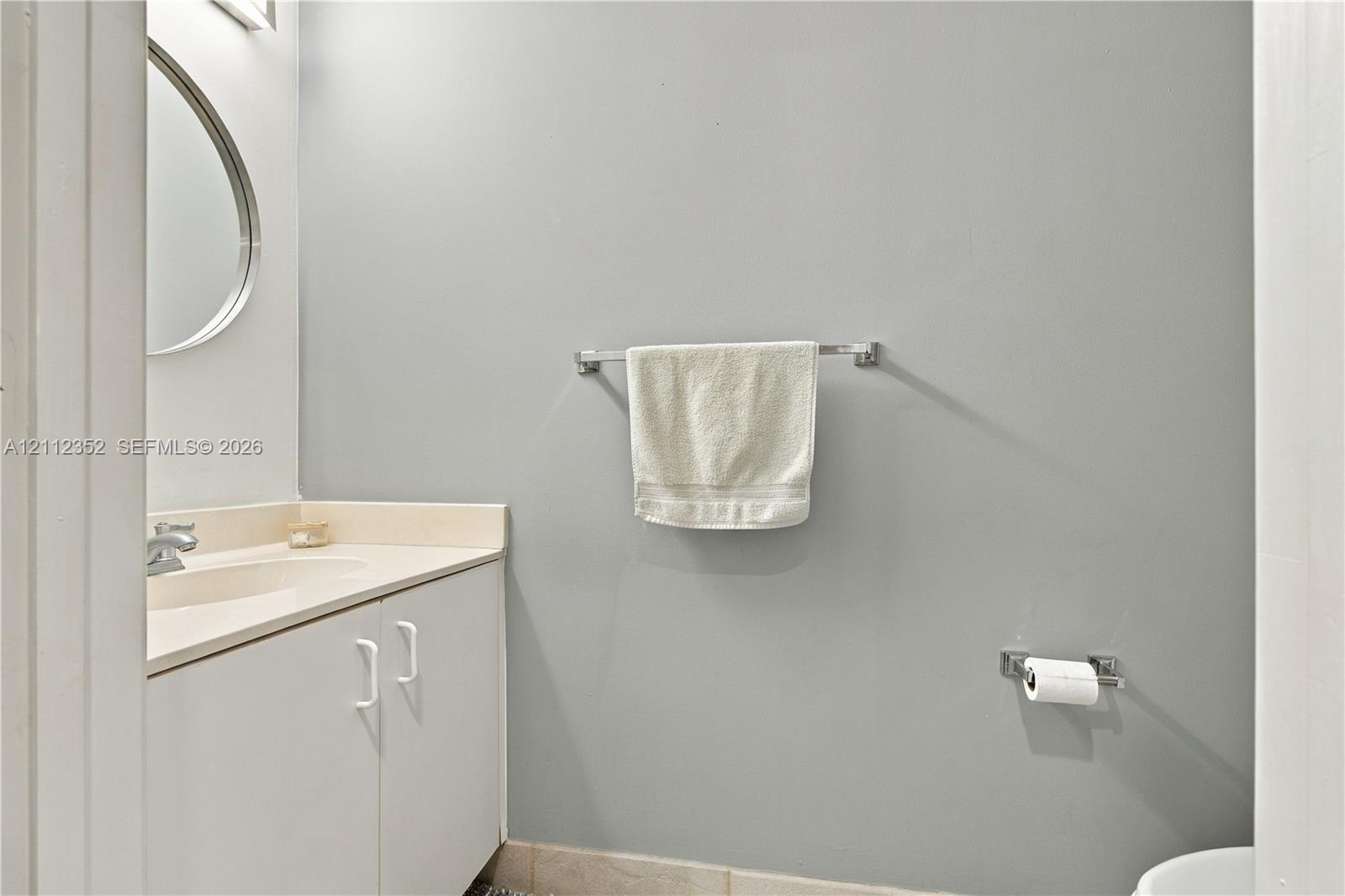 Bathroom featuring a vanity with an integrated sink, polished chrome faucet, wall-mounted circular mirror, and chrome hardware fixtures