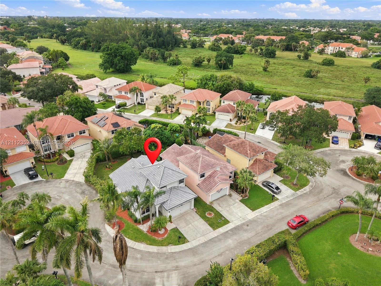 Aerial perspective featuring a tile roof, multi-level architectural design, attached garage, and paved driveway situated within a suburban landscape