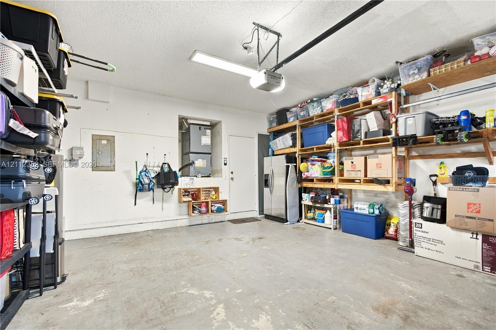 Garage featuring concrete flooring, built-in wall shelving, an overhead automatic door opener, and a dedicated utility closet