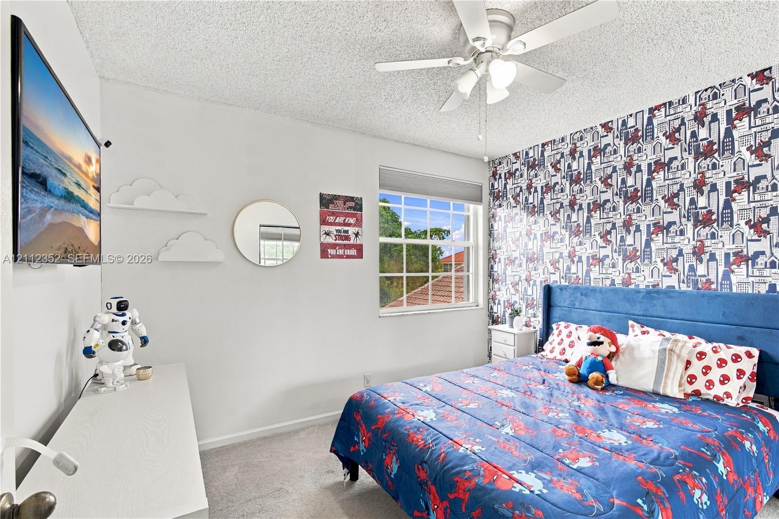 Bedroom featuring a ceiling fan with integrated lighting, a grid-patterned window, and patterned accent wall covering