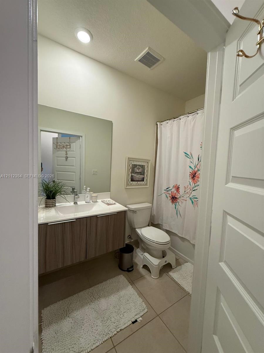 Floating vanity with a light wood-finish cabinet, white countertop, integrated sink, large wall-mounted mirror, and tile flooring