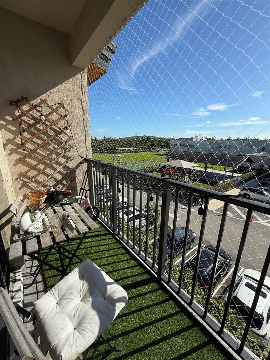Covered balcony featuring synthetic turf flooring, black metal railing, and protective mesh screening