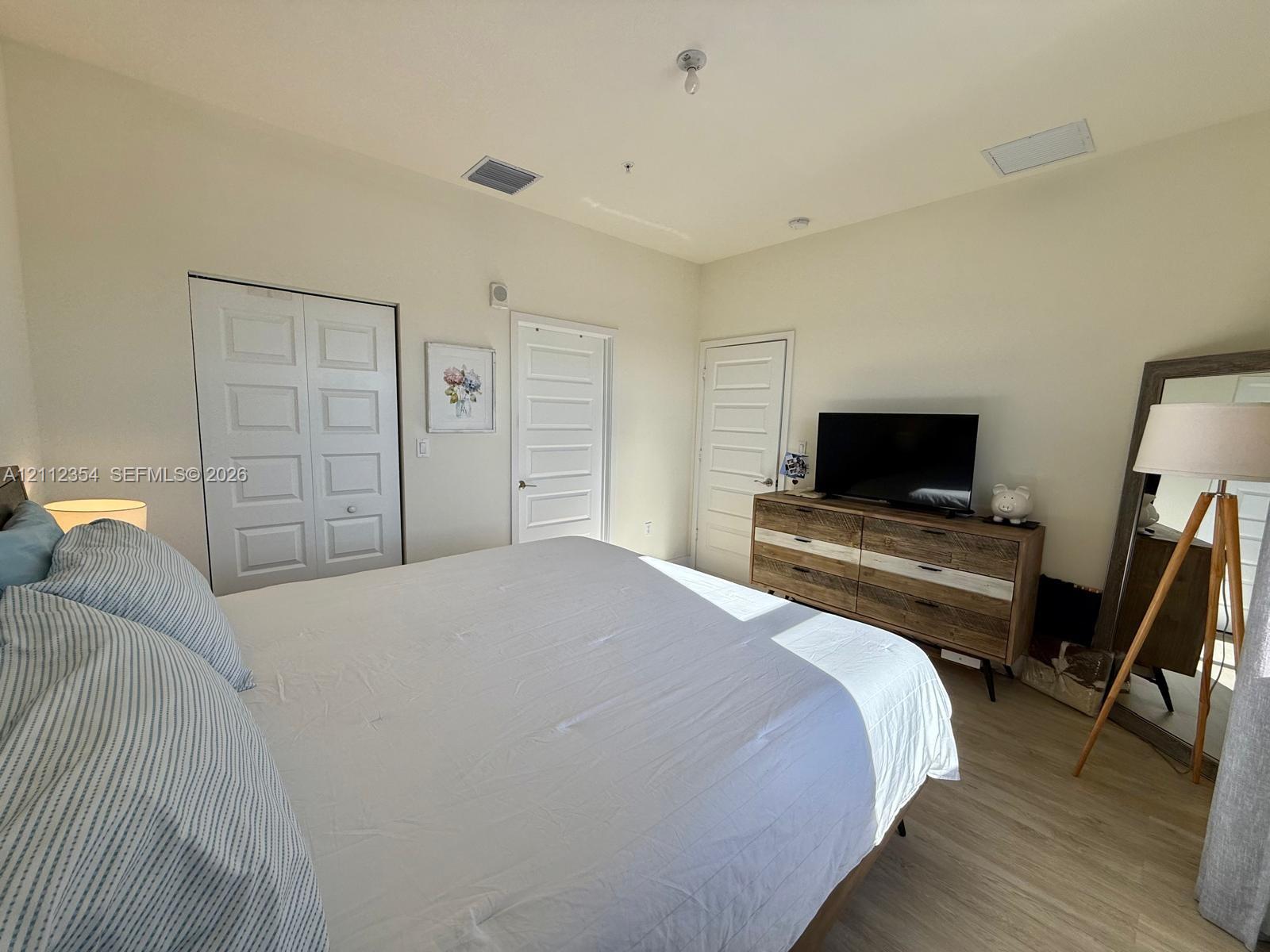 Bedroom featuring wood-finish flooring, high ceilings, neutral wall color, and multiple five-panel interior doors
