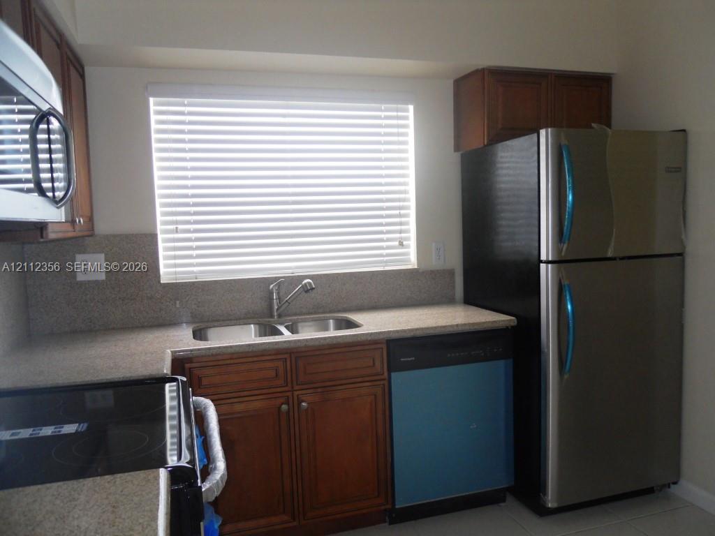 Kitchen featuring wood cabinetry, stone-surface countertops, dual-basin sink, integrated stainless steel appliances, and horizontal window blinds