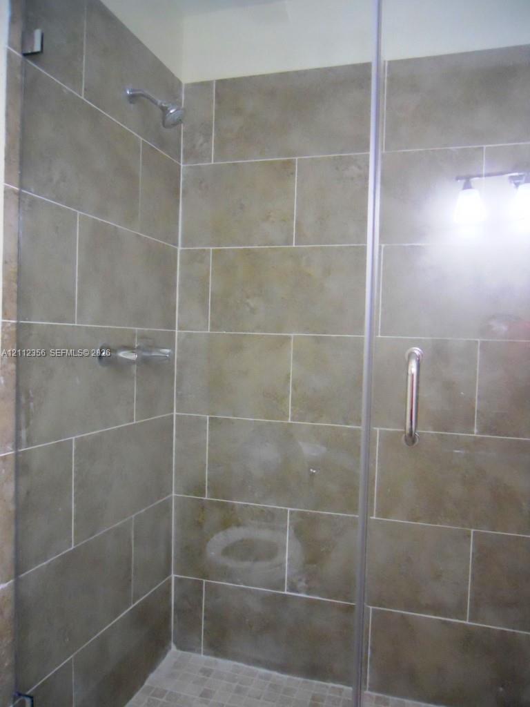Walk-in shower featuring large-format neutral tile wall surround, glass enclosure with brushed metal hardware, wall-mounted showerhead, and mosaic tile flooring