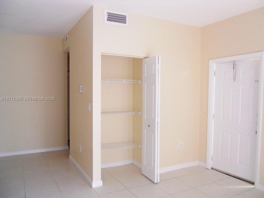 Interior space featuring neutral-toned walls, tile flooring, a six-panel door, and a built-in closet with wire shelving