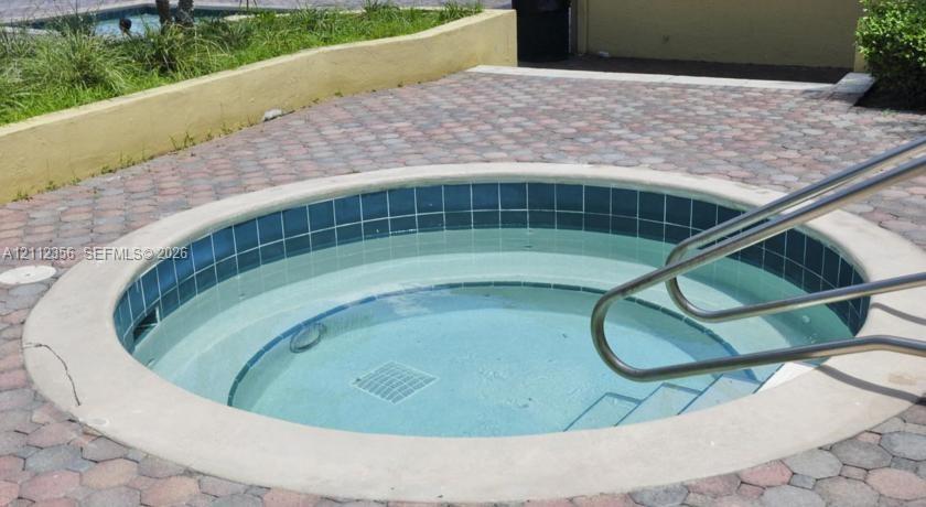 In-ground spa with tile waterline, concrete coping, metal handrail, and paver surround
