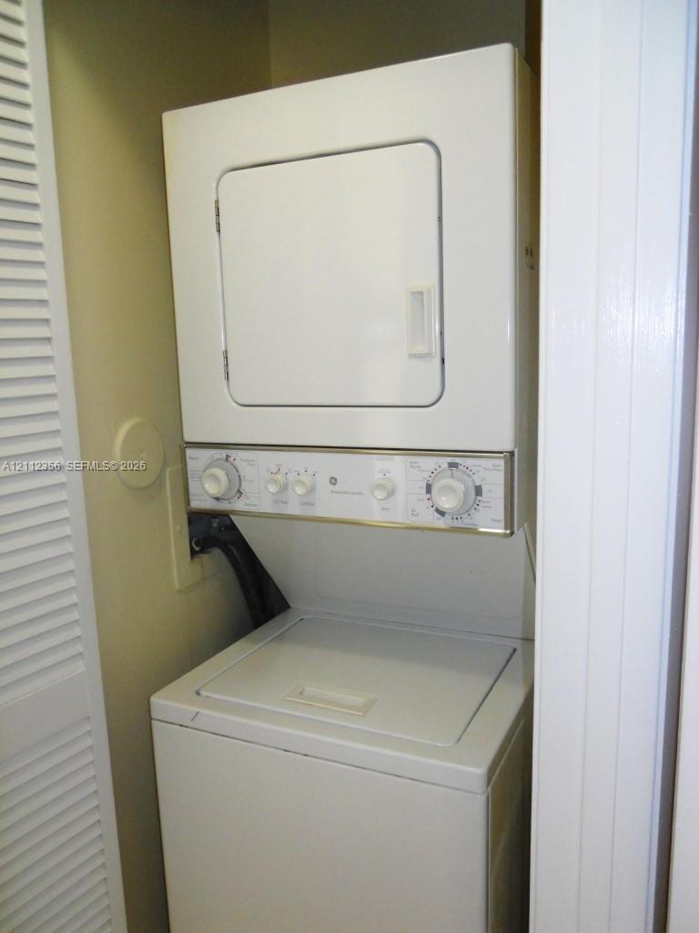 Stacked laundry unit with top-loading washer, front-loading dryer, and white louvered closet door