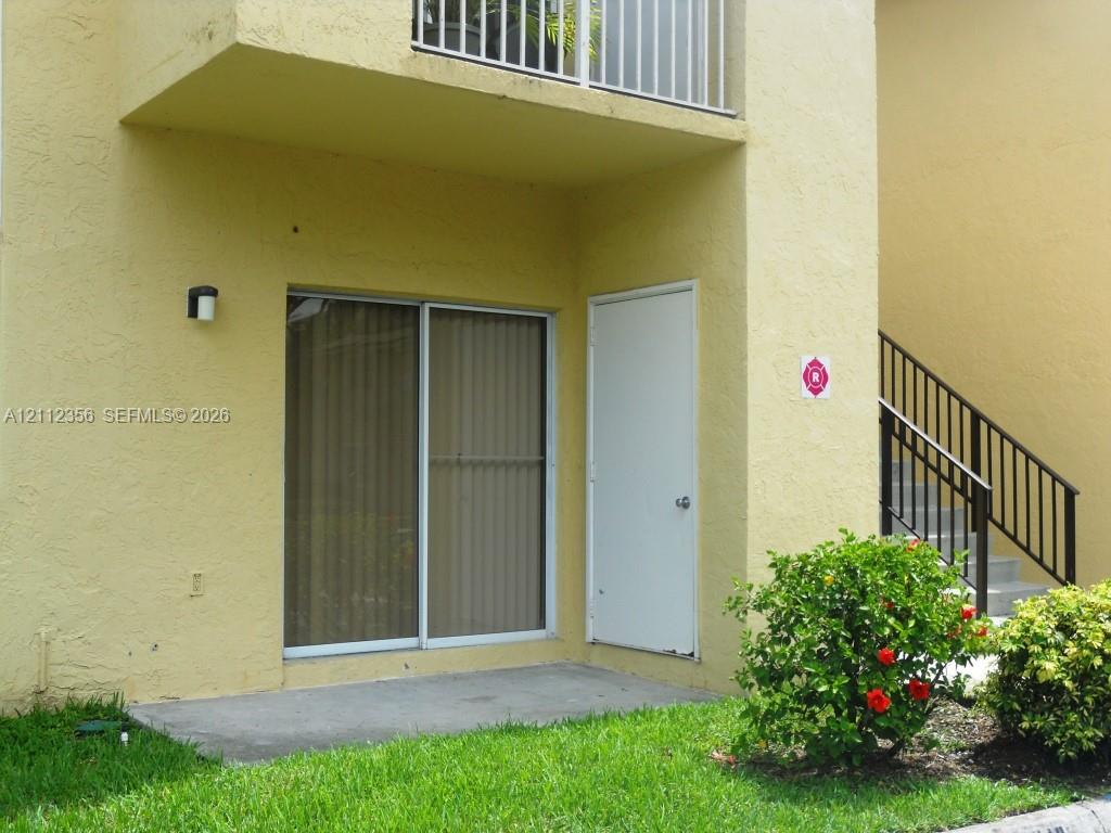 Stucco exterior featuring a concrete patio, sliding glass door, private exterior storage closet, and second-story balcony with metal railing Stucco exterior featuring a concrete patio, sliding glass door, private exterior storage closet, and second-story balcony with metal railing