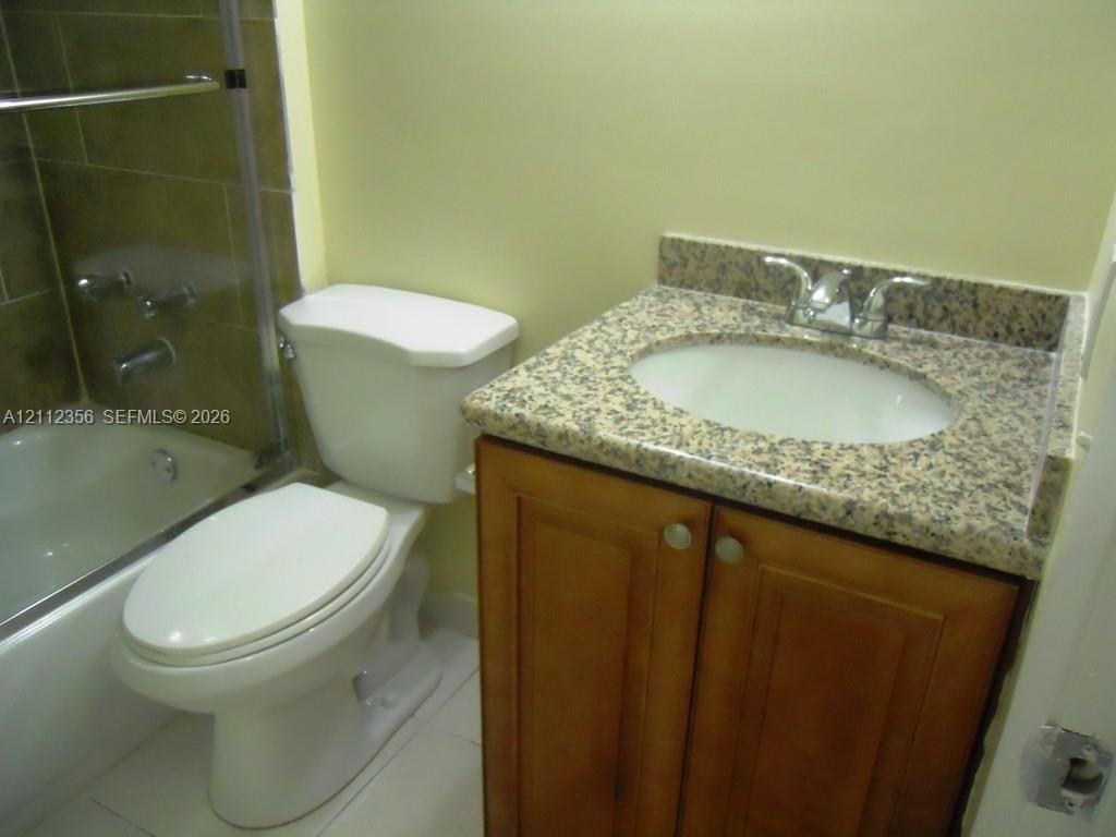 Bathroom featuring a wood-finish vanity with a stone-composite countertop, undermount sink, chrome faucet, and a shower-tub combination with tile surround