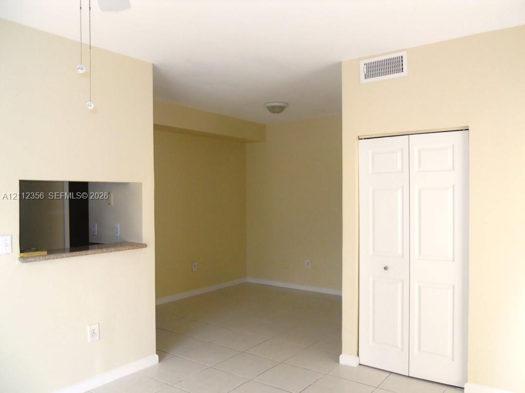 Neutral-toned interior space featuring light-colored tile flooring, a built-in pass-through opening with a stone-finish countertop, and a white bi-fold closet door Neutral-toned interior space featuring light-colored tile flooring, a built-in pass-through opening with a stone-finish countertop, and a white bi-fold closet door