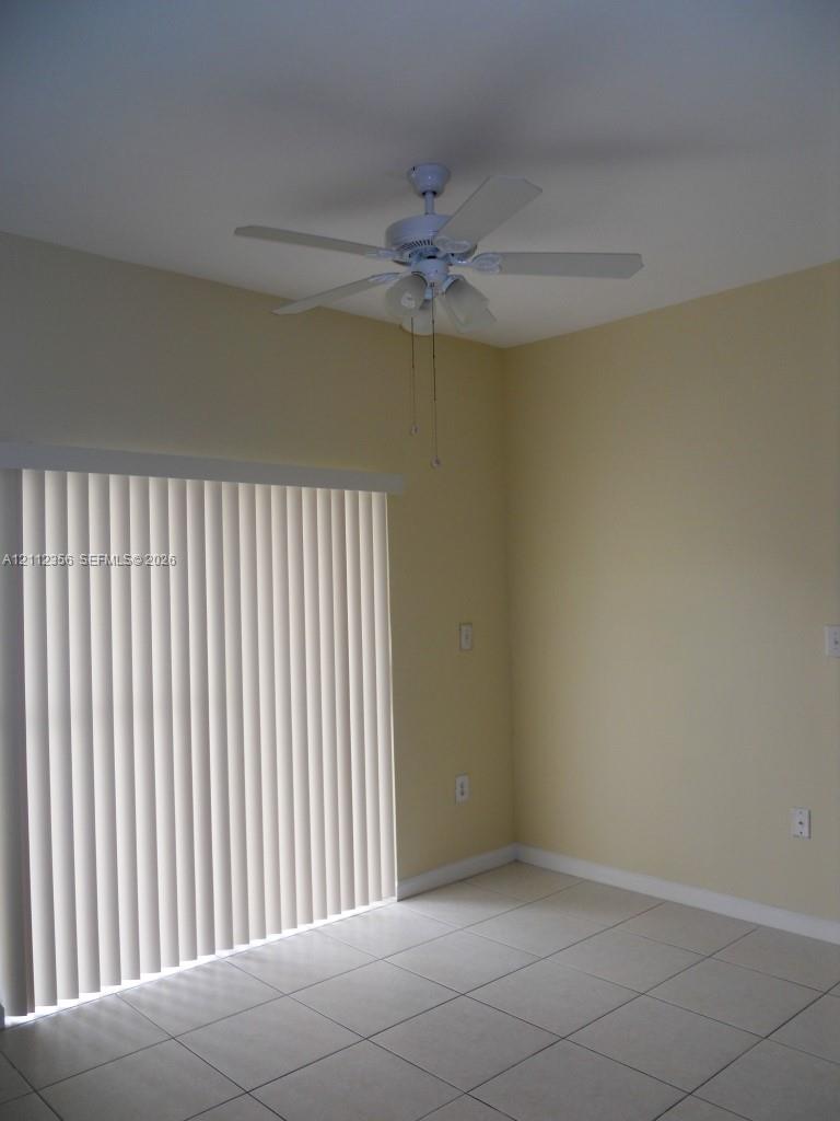 Room featuring ceramic tile flooring, a multi-blade ceiling fan with integrated lighting, and a vertical sliding glass door with blinds Room featuring ceramic tile flooring, a multi-blade ceiling fan with integrated lighting, and a vertical sliding glass door with blinds