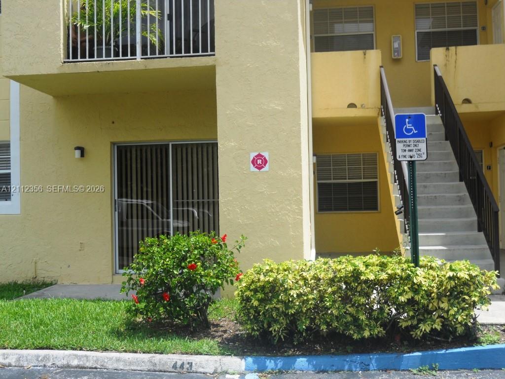 Multi-story exterior featuring stucco siding, sliding glass patio doors, a second-level balcony with metal railings, and concrete stairwell access Multi-story exterior featuring stucco siding, sliding glass patio doors, a second-level balcony with metal railings, and concrete stairwell access