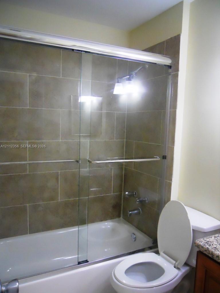 Bathtub featuring a glass sliding door and large-format rectangular wall tile, complemented by a stone-finish countertop