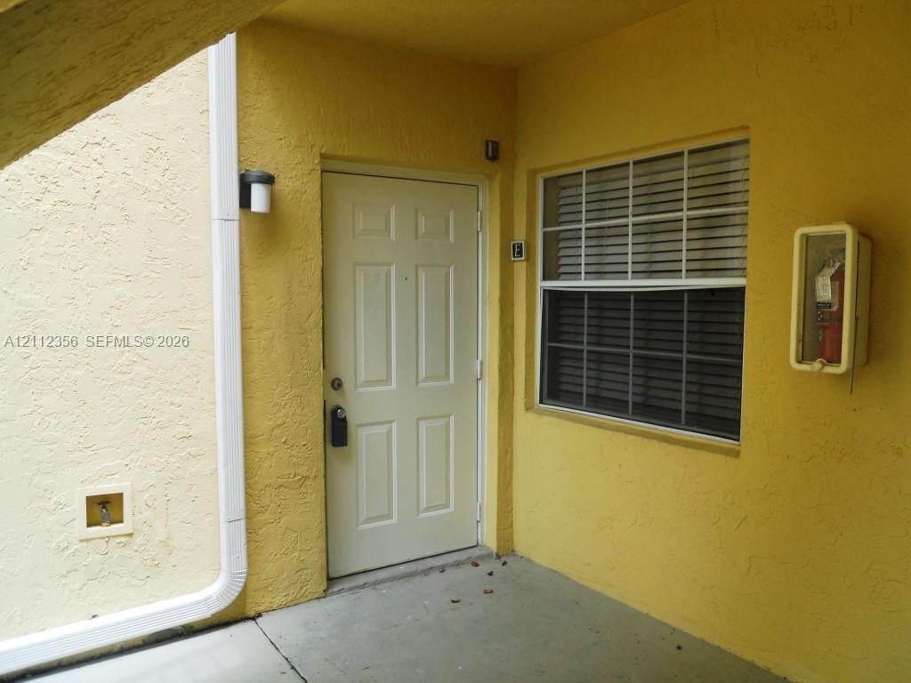 Entryway featuring a solid-panel door, grid-pattern window, stucco exterior finish, wall-mounted light fixture, and recessed utility access Entryway featuring a solid-panel door, grid-pattern window, stucco exterior finish, wall-mounted light fixture, and recessed utility access