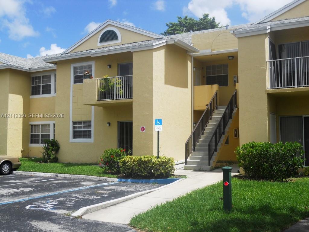 Two-story stucco exterior featuring a gabled roofline, semi-circular attic vent, metal railed balcony, and exterior concrete staircase Two-story stucco exterior featuring a gabled roofline, semi-circular attic vent, metal railed balcony, and exterior concrete staircase