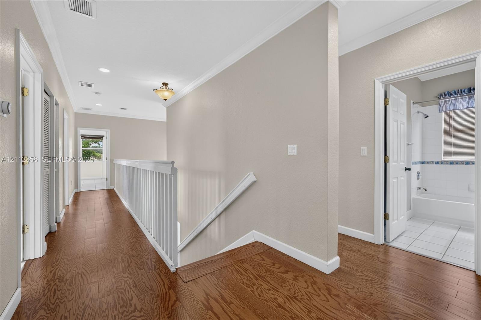Hallway featuring wood-finish flooring, white crown molding, a decorative ceiling-mounted light fixture, and a white balustrade