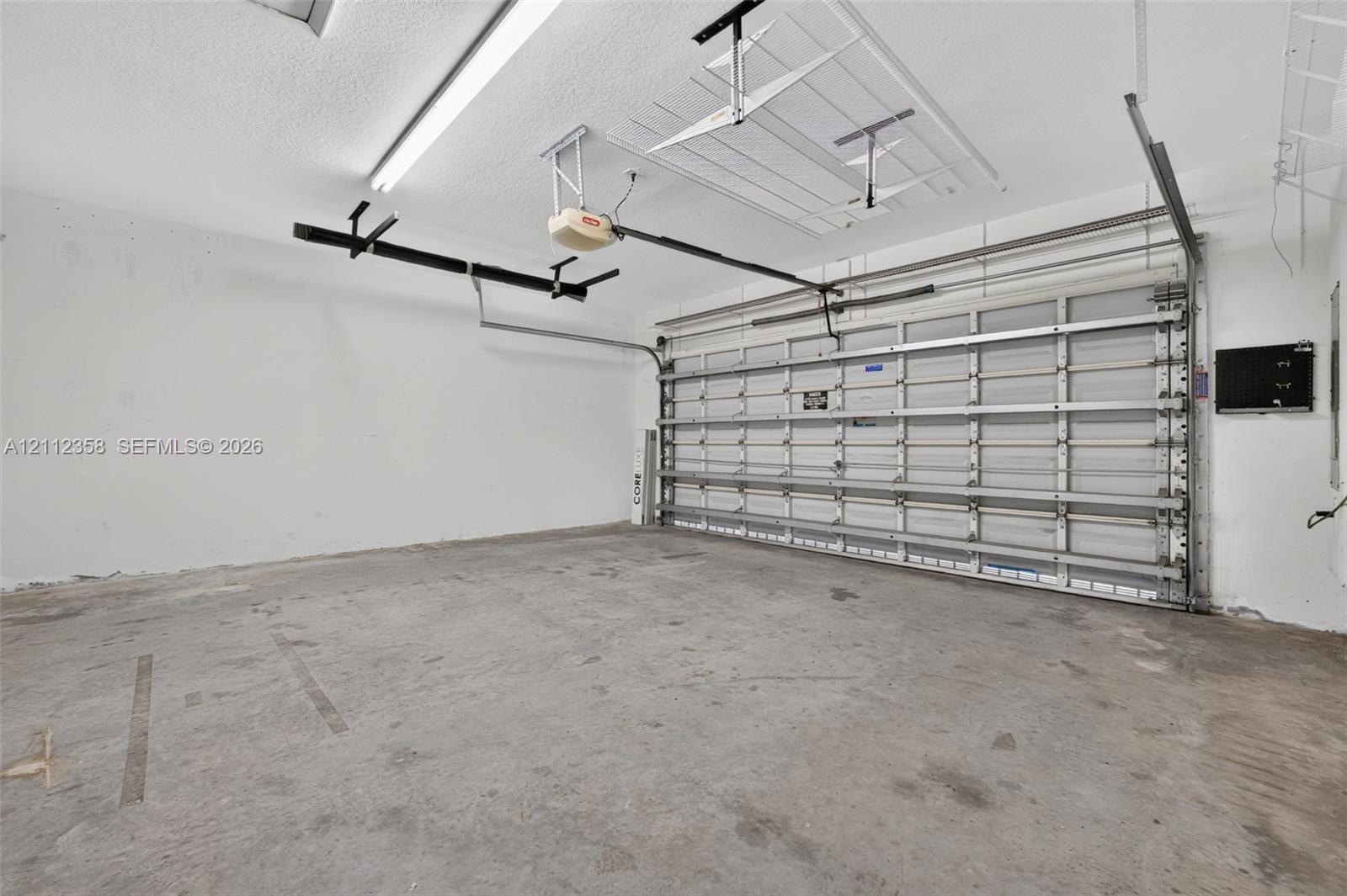 Two-car garage featuring a sectional metal roll-up door, automated door opener, finished interior walls, and overhead lighting