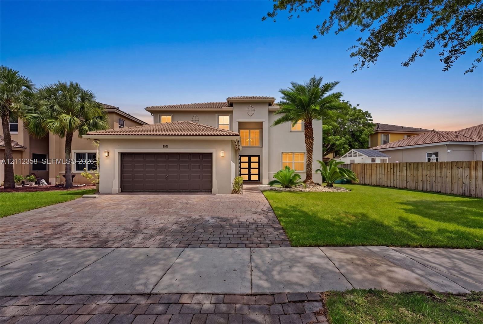 Stucco exterior featuring a tile roof, paved driveway, multi-pane glass entryway, and attached garage