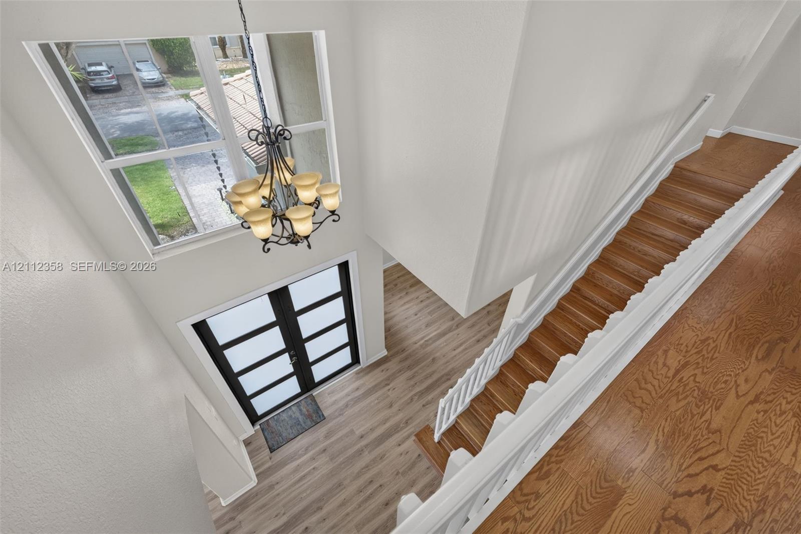 Double-height entryway featuring wood-finish flooring, a multi-pane glass door, a metal chandelier, and a staircase with white balusters