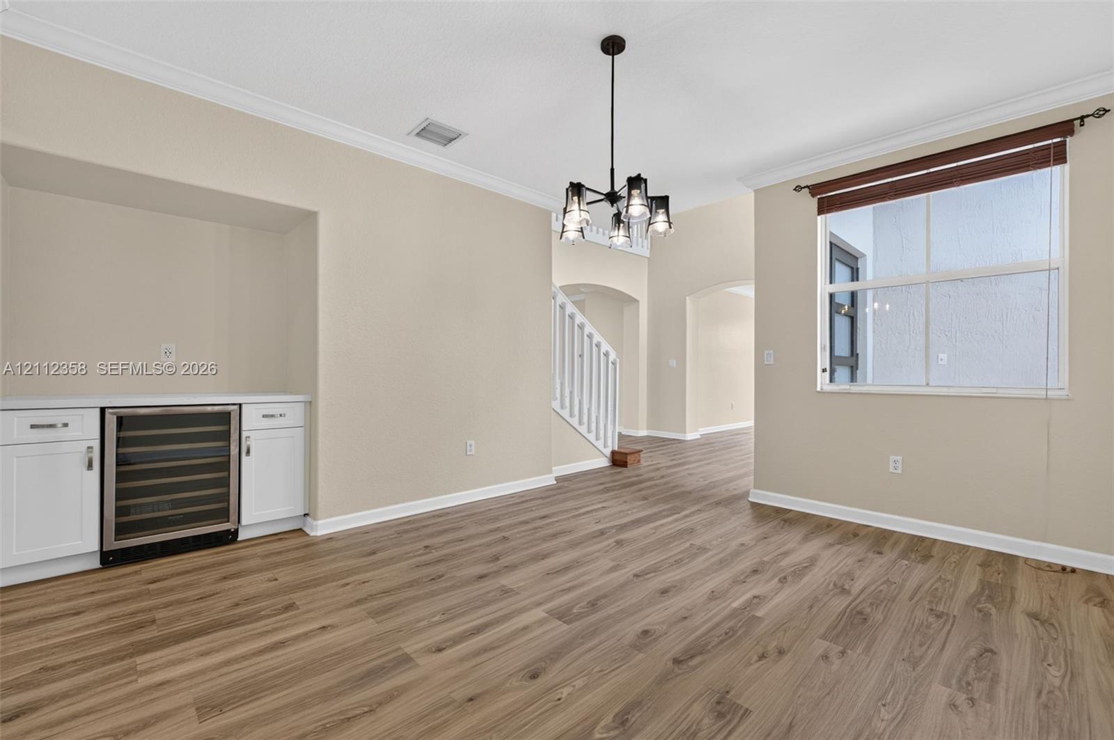 Wood-finish flooring, white built-in cabinetry, integrated wine refrigerator, multi-arm chandelier, and crown molding
