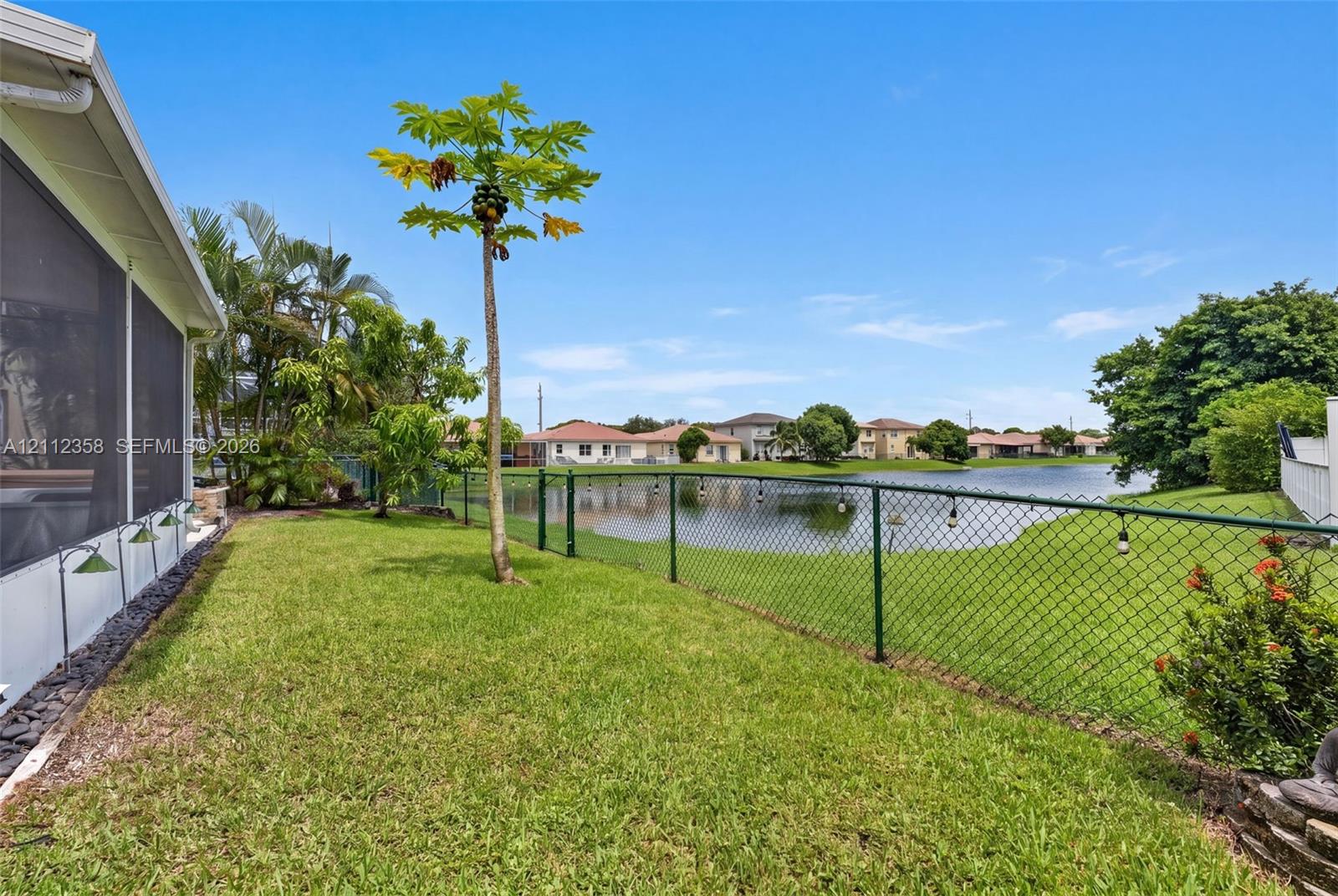 Backyard featuring a manicured lawn, water frontage, metal chain-link fencing, and mature landscaping